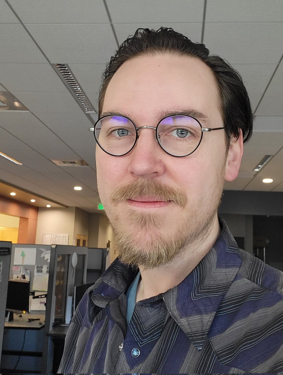 Selfie of a man with brown hair and glasses standing in an office.